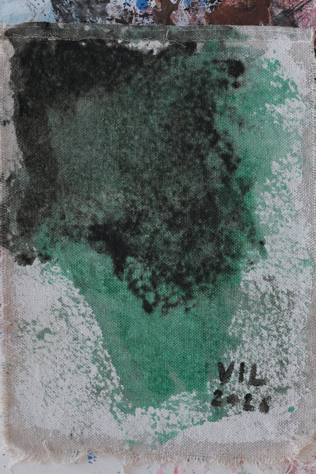 An abstract square art print or canvas featuring a textured wash of green and dark charcoal gray on a white ground, presented on a heavily splattered multicolor artist's palette background.